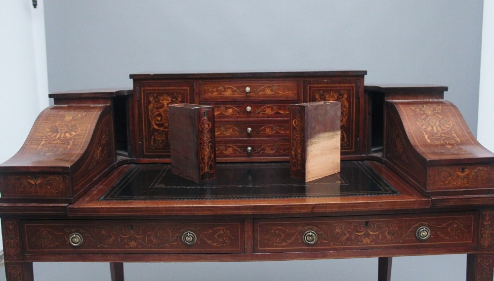 A pair of early 20th-century mahogany Carlton House desks with detailed satinwood marquetry inlay, stepped gallery drawers, and tapered legs. View XXII