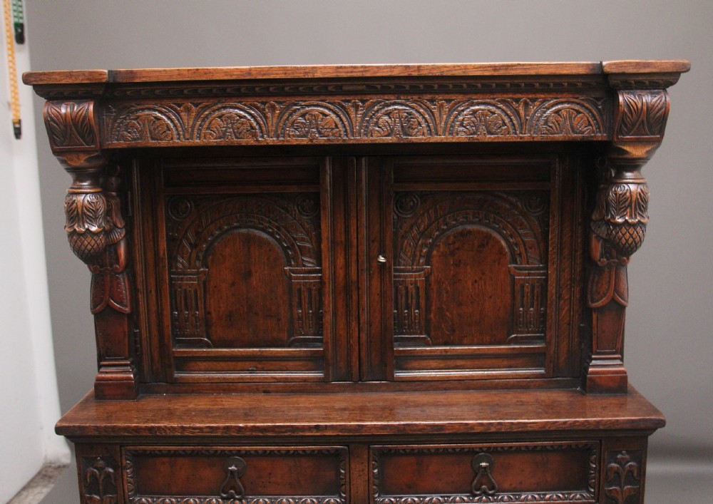 A carved dark oak court cupboard featuring arcaded door panels, turned bulbous supports, and geometric inlay details. View III