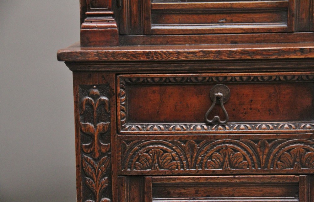 A carved dark oak court cupboard featuring arcaded door panels, turned bulbous supports, and geometric inlay details. View IV