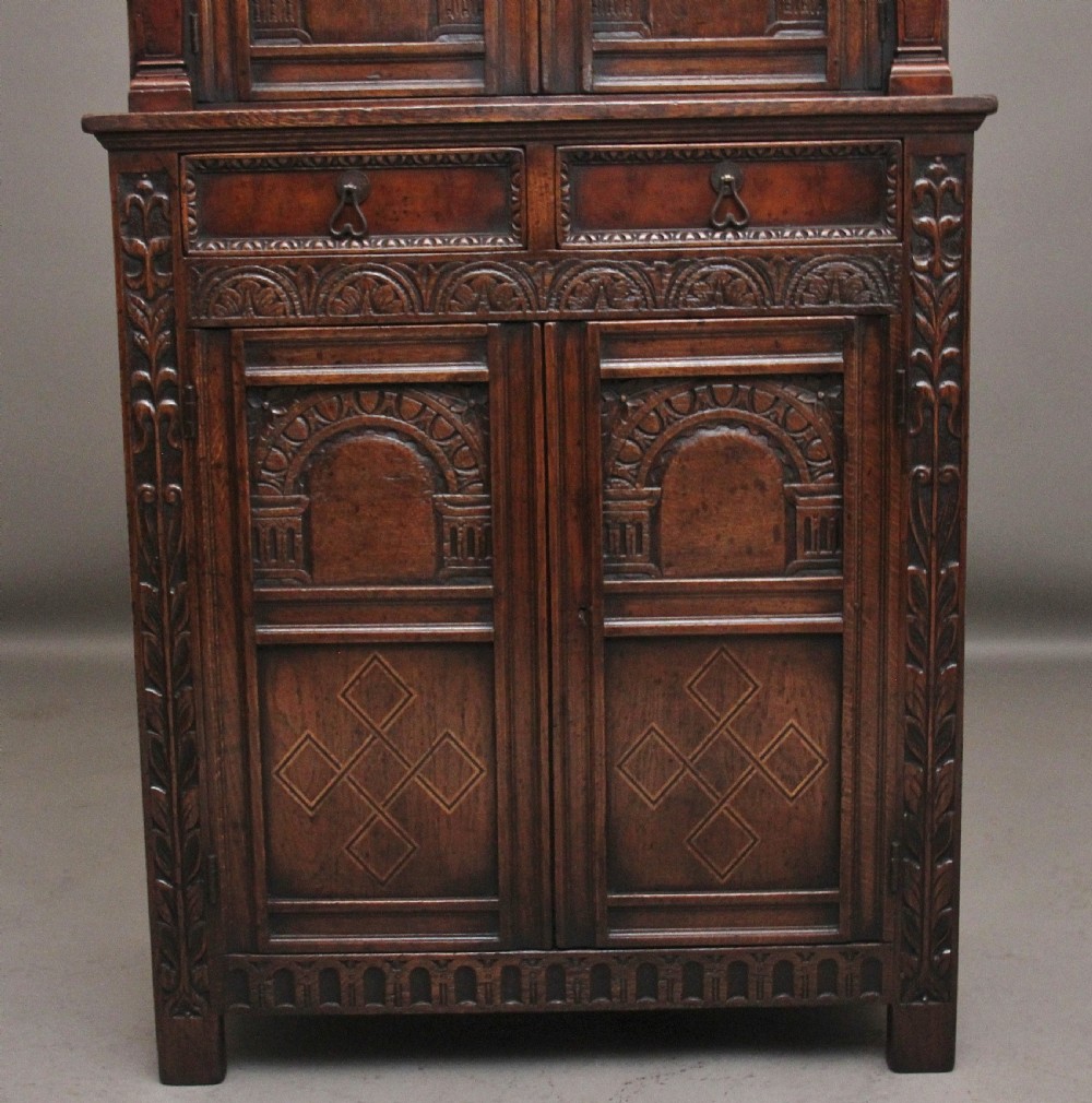 A carved dark oak court cupboard featuring arcaded door panels, turned bulbous supports, and geometric inlay details. View V