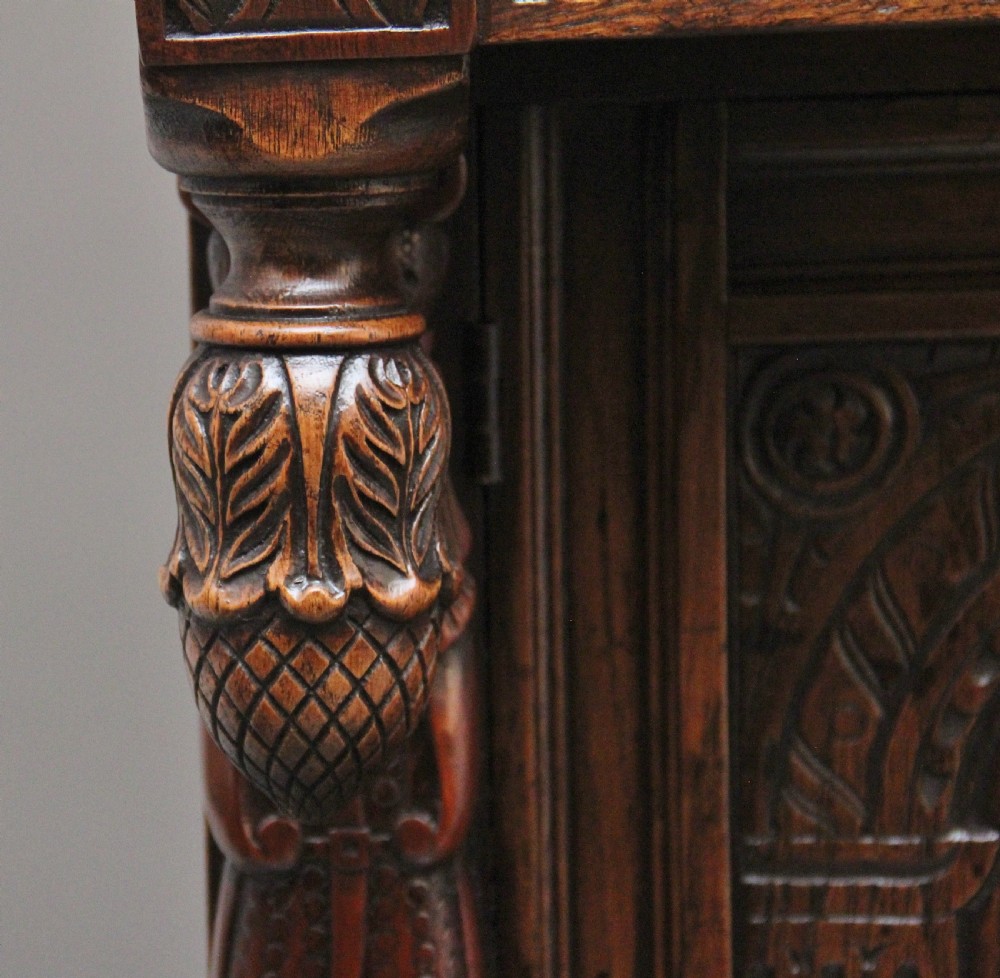 A carved dark oak court cupboard featuring arcaded door panels, turned bulbous supports, and geometric inlay details. View VI