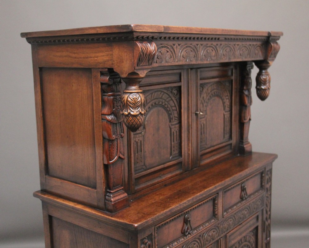 A carved dark oak court cupboard featuring arcaded door panels, turned bulbous supports, and geometric inlay details. View VII