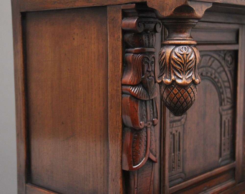 A carved dark oak court cupboard featuring arcaded door panels, turned bulbous supports, and geometric inlay details. View VIII