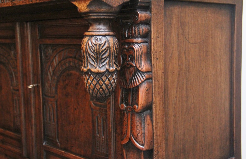 A carved dark oak court cupboard featuring arcaded door panels, turned bulbous supports, and geometric inlay details. View IX