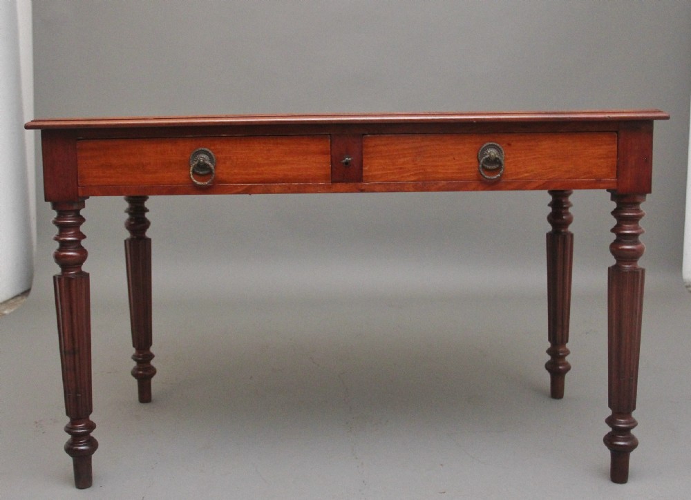 A 19th-century mahogany writing table featuring two frieze drawers with brass ring drop handles, supported by four turned and reeded legs.