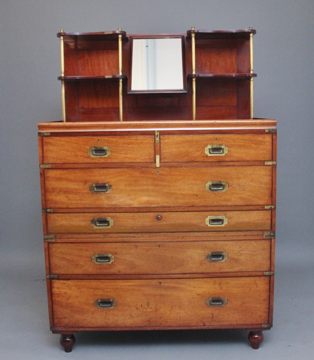 A 19th-century mahogany campaign chest of drawers featuring brass corner brackets, flush brass handles, turned feet, and an upper shelf superstructure with a central mirror.