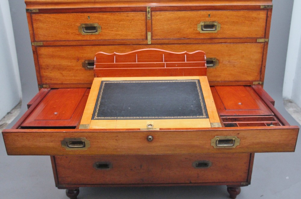 A 19th-century mahogany campaign chest of drawers featuring brass corner brackets, flush brass handles, turned feet, and an upper shelf superstructure with a central mirror. View V