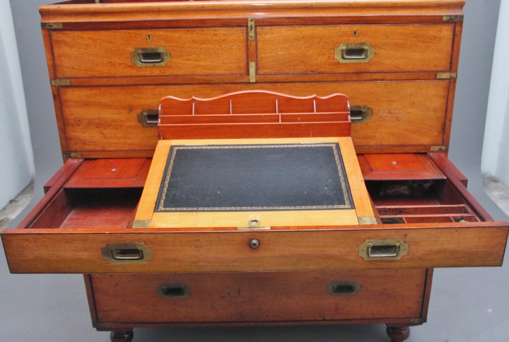 A 19th-century mahogany campaign chest of drawers featuring brass corner brackets, flush brass handles, turned feet, and an upper shelf superstructure with a central mirror. View VII