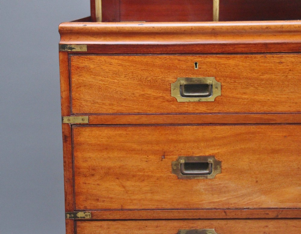 A 19th-century mahogany campaign chest of drawers featuring brass corner brackets, flush brass handles, turned feet, and an upper shelf superstructure with a central mirror. View VIII
