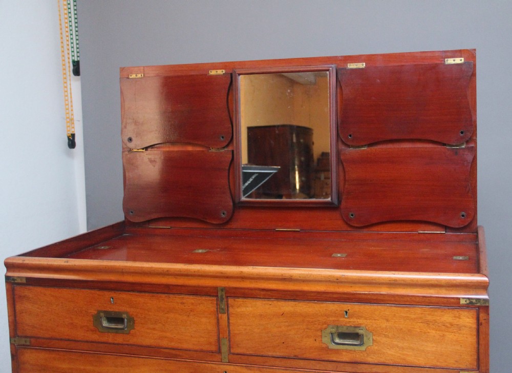 A 19th-century mahogany campaign chest of drawers featuring brass corner brackets, flush brass handles, turned feet, and an upper shelf superstructure with a central mirror. View X
