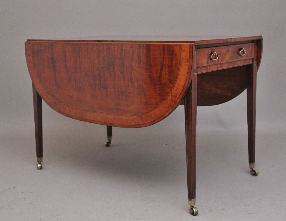 An early 19th-century inlaid mahogany Pembroke table with rounded drop leaves, a single frieze drawer, tapered legs, and brass castors.