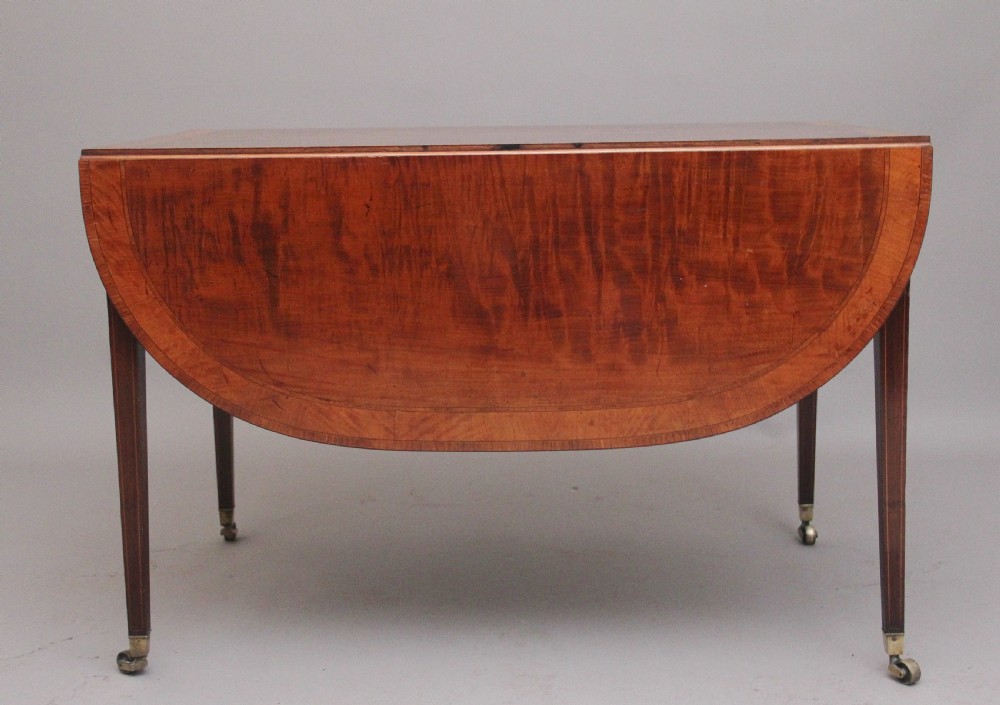 An early 19th-century inlaid mahogany Pembroke table with rounded drop leaves, a single frieze drawer, tapered legs, and brass castors. View V