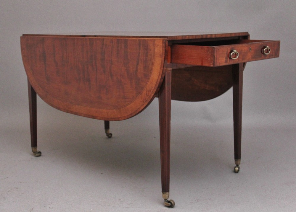 An early 19th-century inlaid mahogany Pembroke table with rounded drop leaves, a single frieze drawer, tapered legs, and brass castors. View X