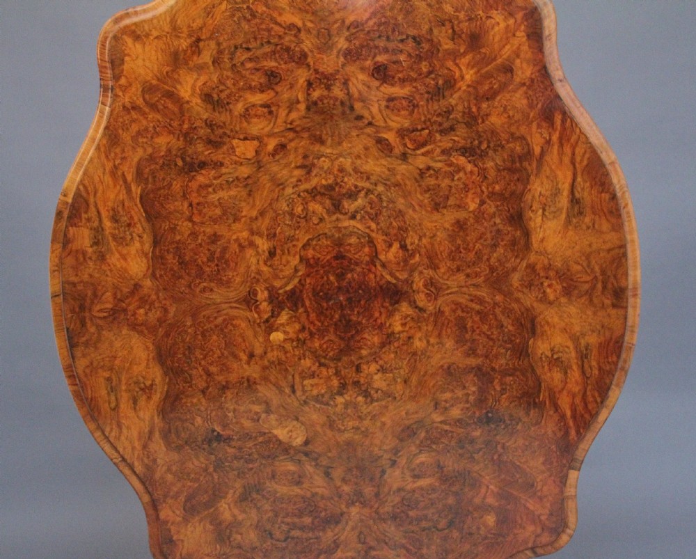 A 19th-century Victorian burr walnut centre table with a shaped, highly figured tilt-top top, raised on a carved pedestal with four cabriole legs on brass castors. View III