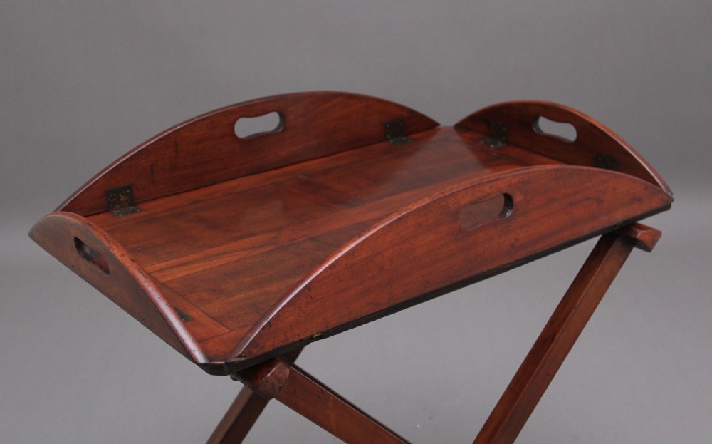 A 19th-century mahogany butler tray featuring shaped gallery sides with cutout handles resting upon a collapsible X-frame stand with webbing straps. View IV