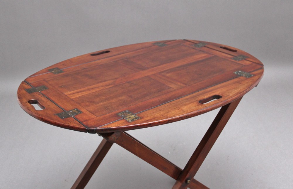 A 19th-century mahogany butler tray featuring shaped gallery sides with cutout handles resting upon a collapsible X-frame stand with webbing straps. View V
