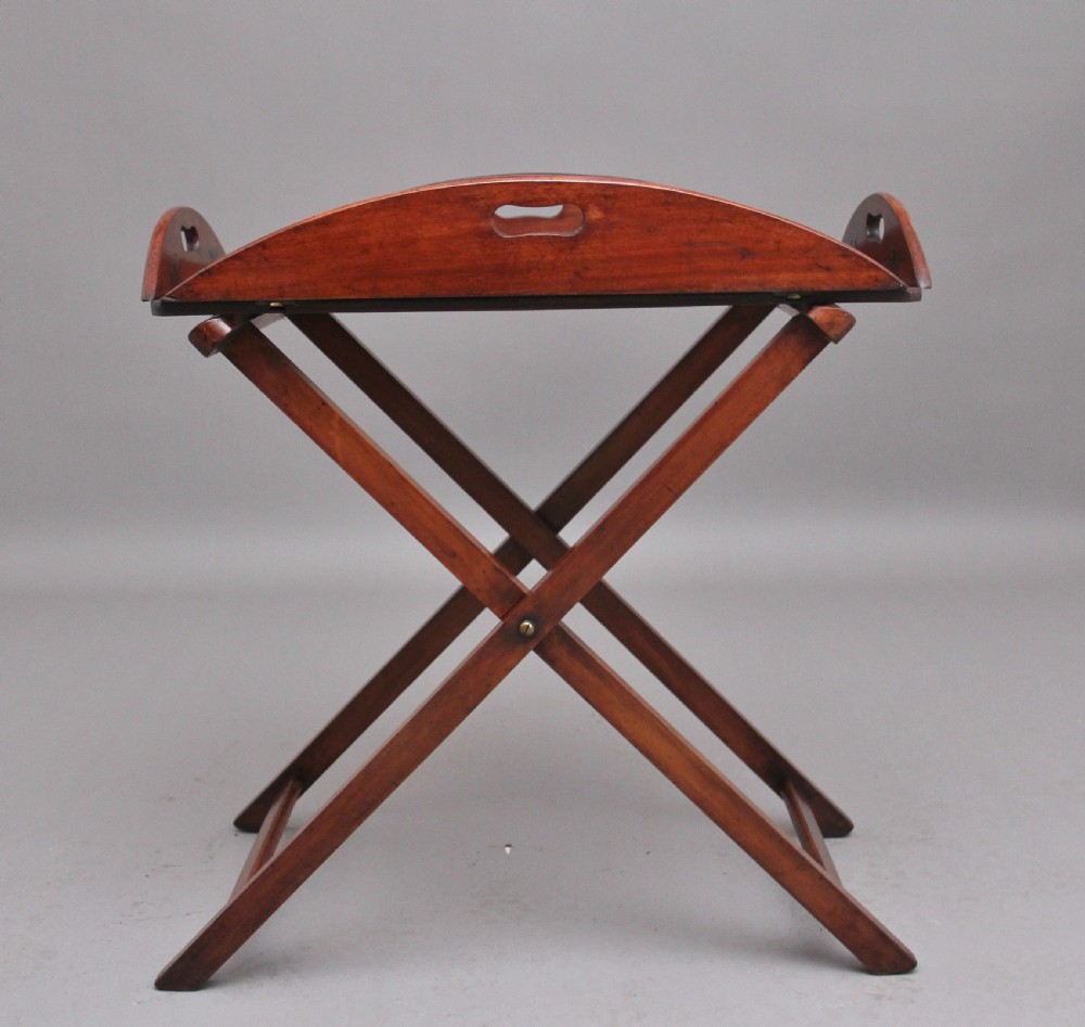 A 19th-century mahogany butler tray featuring shaped gallery sides with cutout handles resting upon a collapsible X-frame stand with webbing straps. View VII