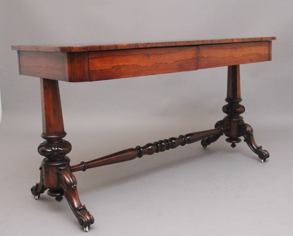 A nineteenth-century dark rosewood library table featuring two frieze drawers, turned trestle supports, a central stretcher, and scroll feet on brass castors. View II