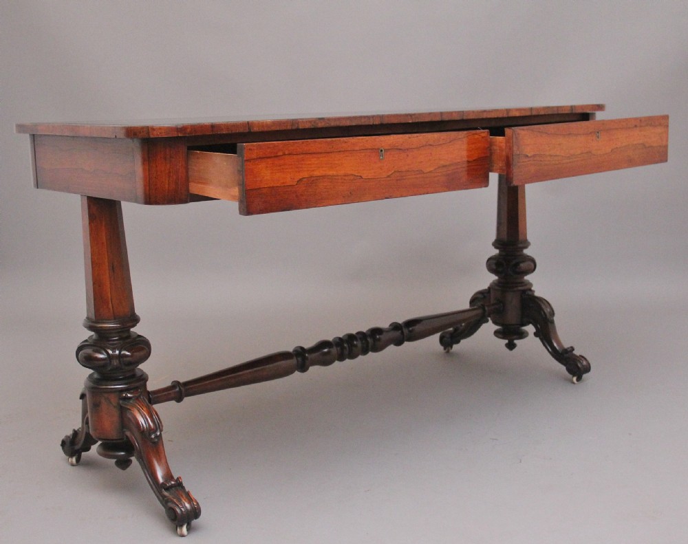 A nineteenth-century dark rosewood library table featuring two frieze drawers, turned trestle supports, a central stretcher, and scroll feet on brass castors. View III