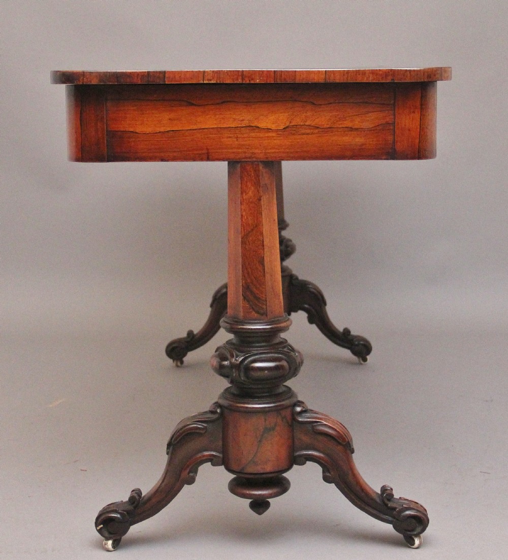 A nineteenth-century dark rosewood library table featuring two frieze drawers, turned trestle supports, a central stretcher, and scroll feet on brass castors. View V