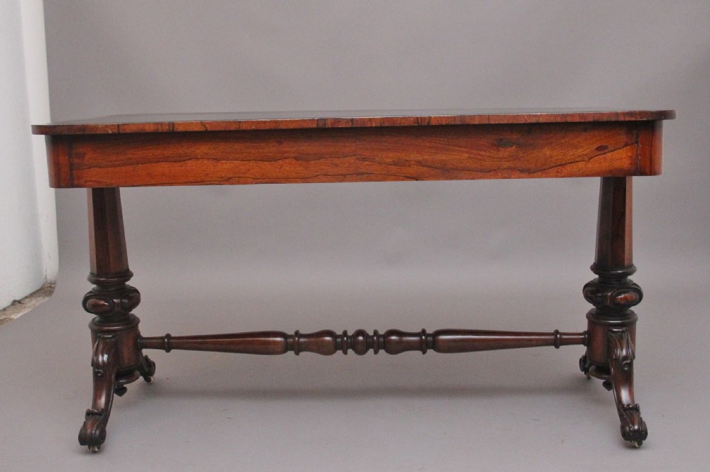 A nineteenth-century dark rosewood library table featuring two frieze drawers, turned trestle supports, a central stretcher, and scroll feet on brass castors. View VI