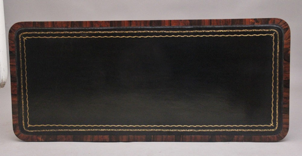 A nineteenth-century dark rosewood library table featuring two frieze drawers, turned trestle supports, a central stretcher, and scroll feet on brass castors. View VIII