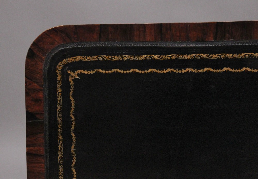 A nineteenth-century dark rosewood library table featuring two frieze drawers, turned trestle supports, a central stretcher, and scroll feet on brass castors. View IX