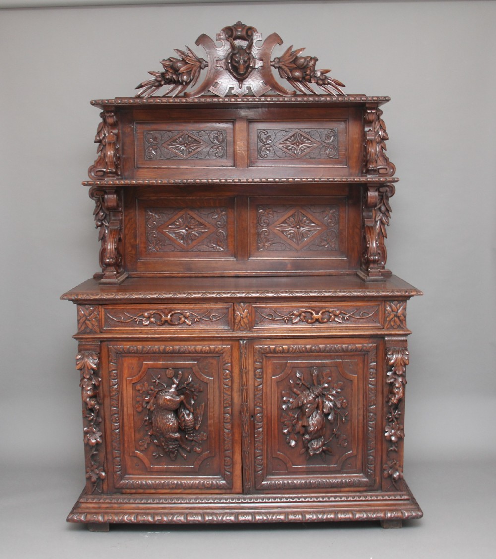 A 19th-century dark oak two-tiered buffet featuring intricate hand-carved reliefs of game, foliage, and a prominent stag head cresting.