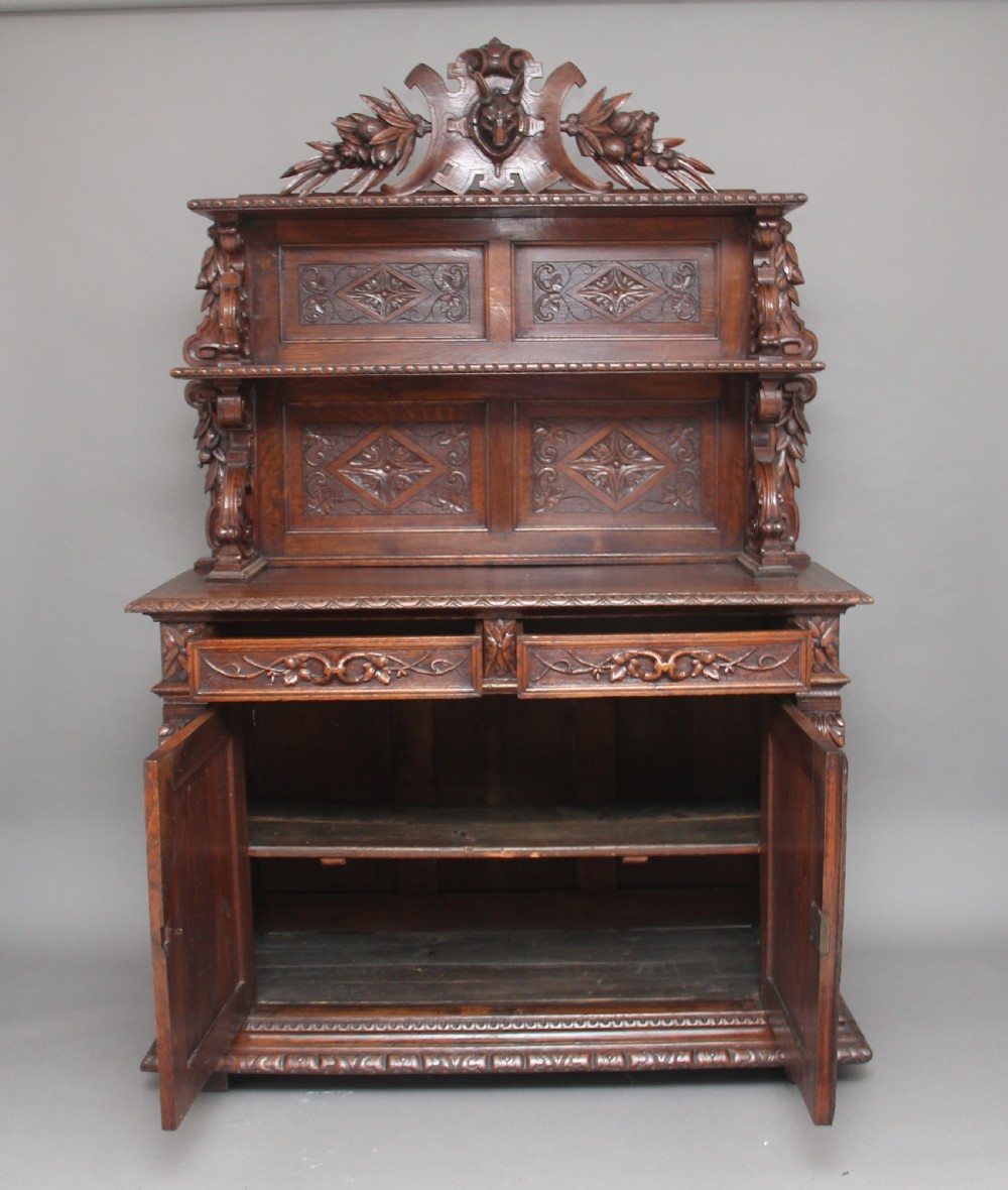 A 19th-century dark oak two-tiered buffet featuring intricate hand-carved reliefs of game, foliage, and a prominent stag head cresting. View II