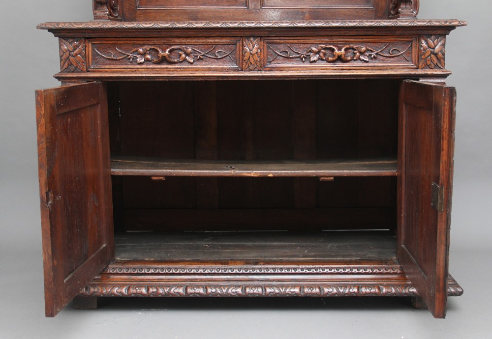 A 19th-century dark oak two-tiered buffet featuring intricate hand-carved reliefs of game, foliage, and a prominent stag head cresting. View V
