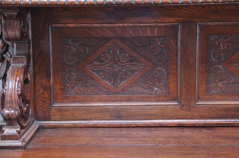 A 19th-century dark oak two-tiered buffet featuring intricate hand-carved reliefs of game, foliage, and a prominent stag head cresting. View XIV
