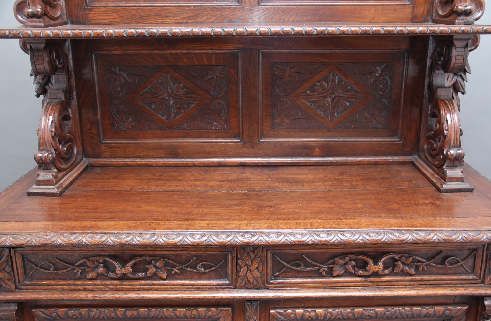 A 19th-century dark oak two-tiered buffet featuring intricate hand-carved reliefs of game, foliage, and a prominent stag head cresting. View XV