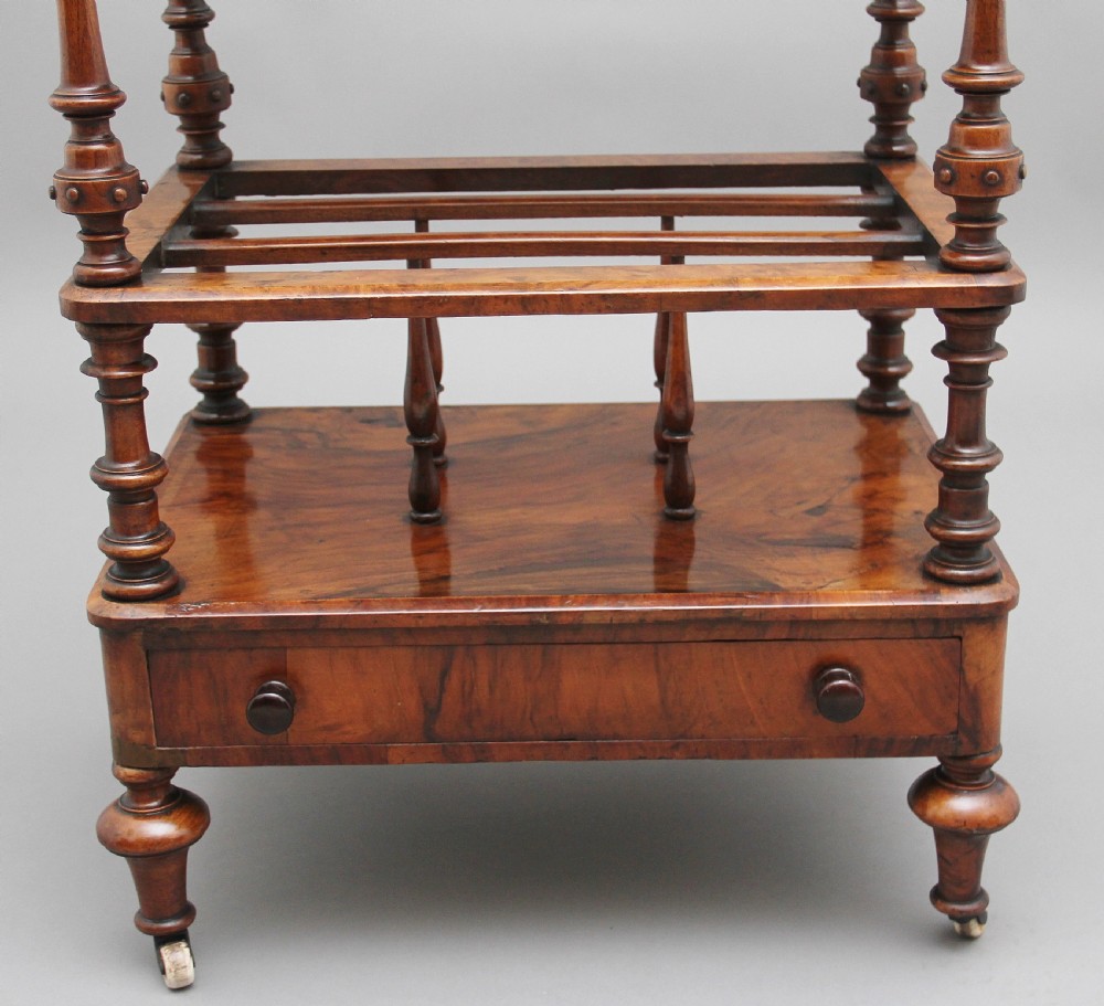 A Victorian burr walnut Canterbury featuring a flat top surface, open slatted partitions, a single base drawer, turned supports, and ceramic castors. View IX