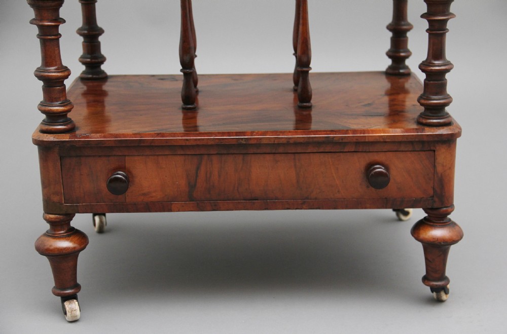 A Victorian burr walnut Canterbury featuring a flat top surface, open slatted partitions, a single base drawer, turned supports, and ceramic castors. View X