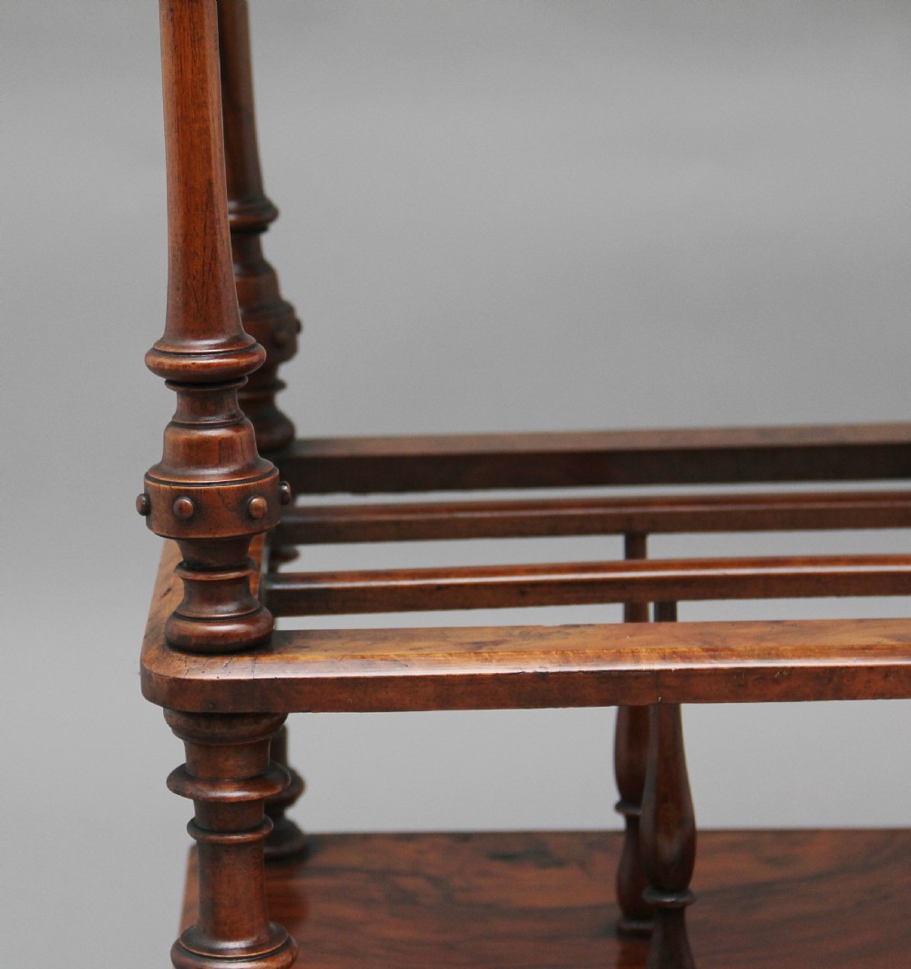 A Victorian burr walnut Canterbury featuring a flat top surface, open slatted partitions, a single base drawer, turned supports, and ceramic castors. View XI