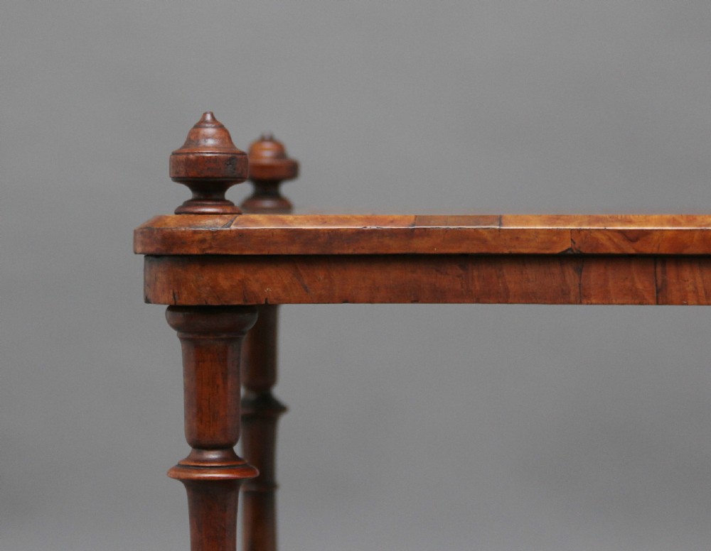 A Victorian burr walnut Canterbury featuring a flat top surface, open slatted partitions, a single base drawer, turned supports, and ceramic castors. View XIII