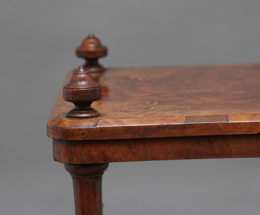 A Victorian burr walnut Canterbury featuring a flat top surface, open slatted partitions, a single base drawer, turned supports, and ceramic castors. View XIV