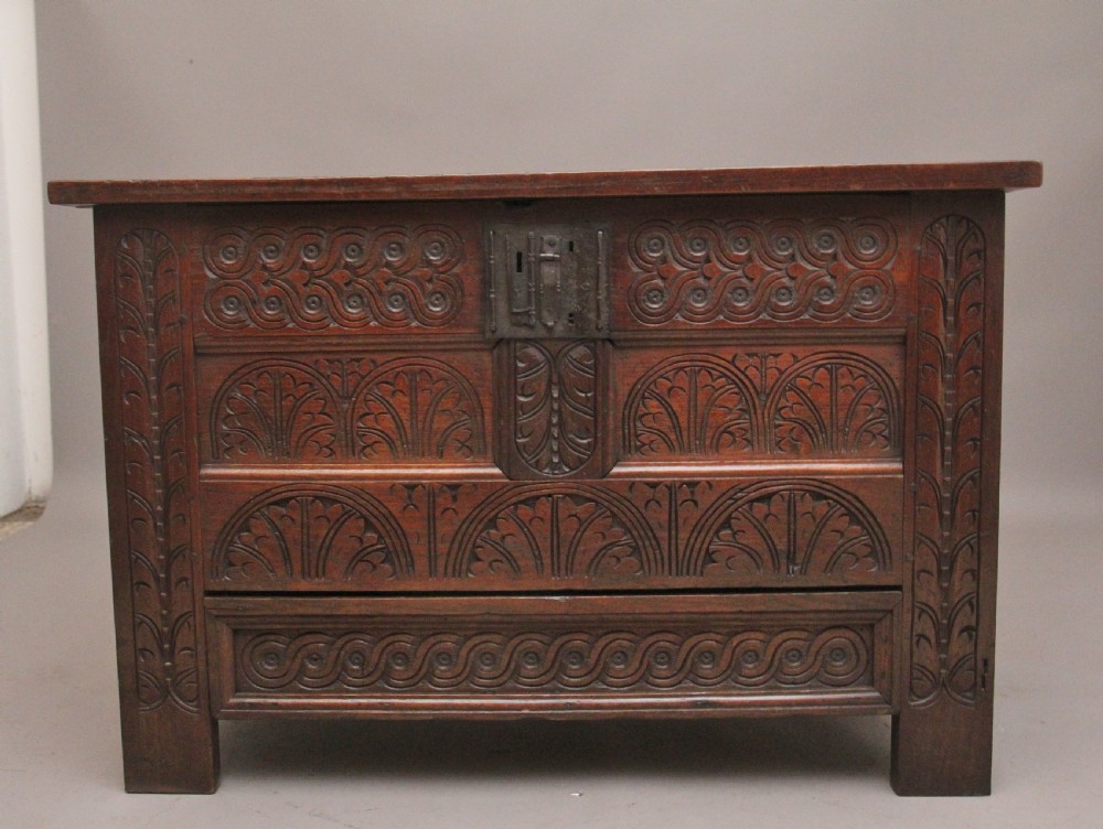 An 18th-century dark carved oak mule chest featuring intricate geometric panel carvings, a central iron lockplate, and a single lower drawer.