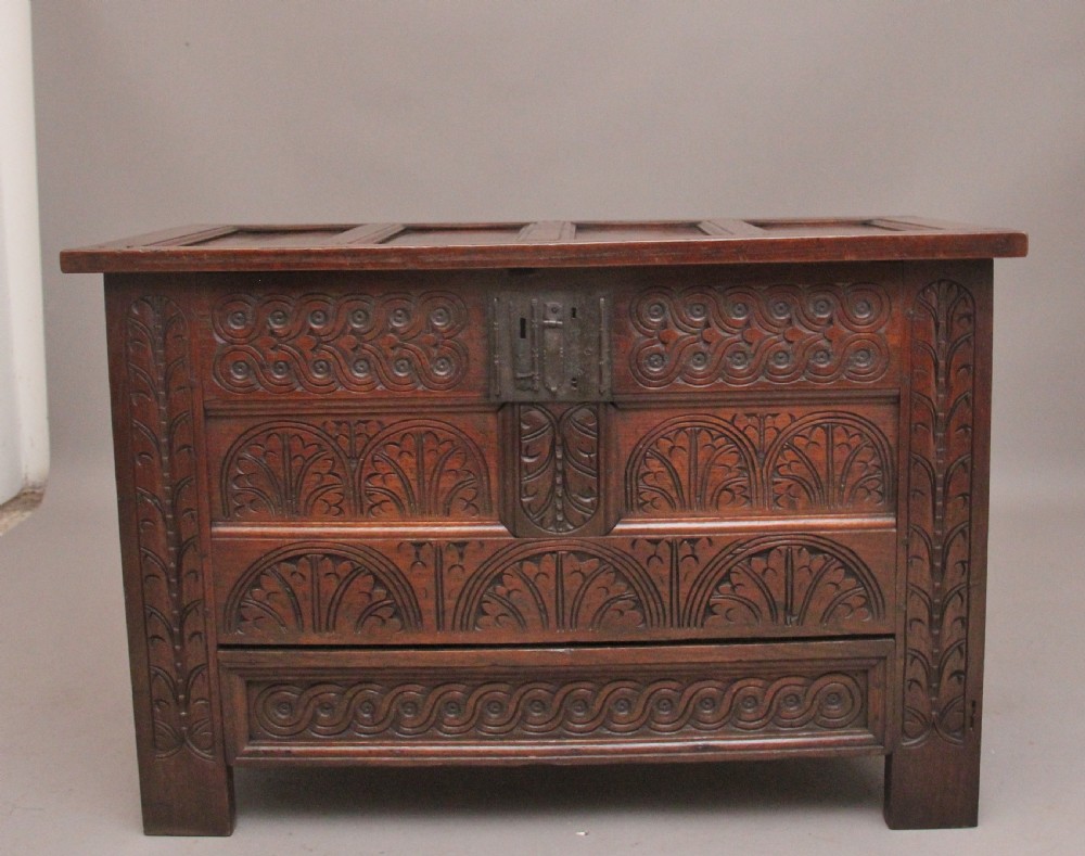 An 18th-century dark carved oak mule chest featuring intricate geometric panel carvings, a central iron lockplate, and a single lower drawer. View II