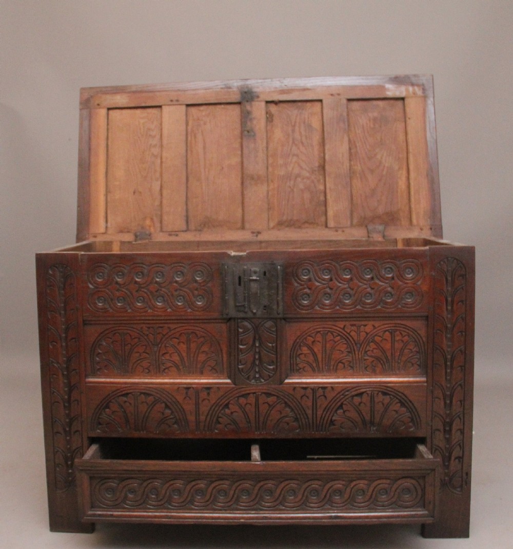 An 18th-century dark carved oak mule chest featuring intricate geometric panel carvings, a central iron lockplate, and a single lower drawer. View IV