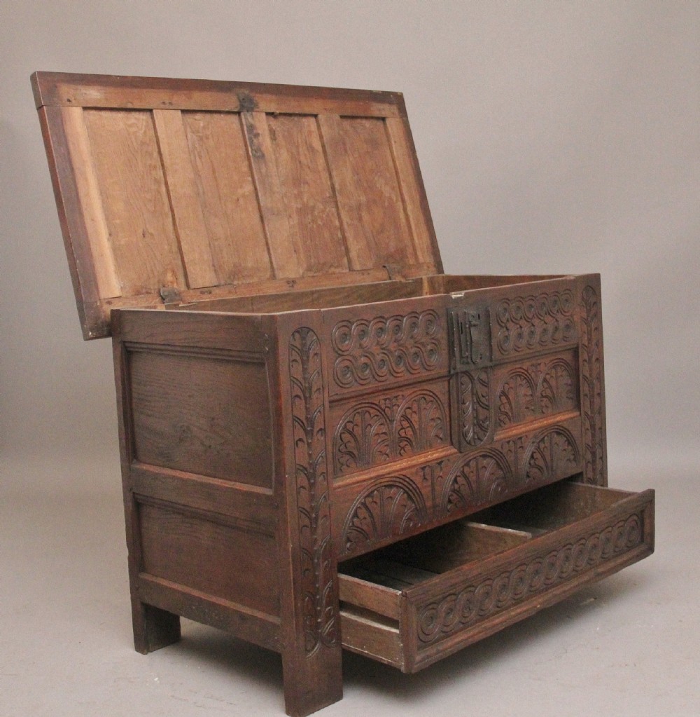 An 18th-century dark carved oak mule chest featuring intricate geometric panel carvings, a central iron lockplate, and a single lower drawer. View V