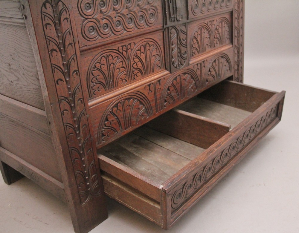 An 18th-century dark carved oak mule chest featuring intricate geometric panel carvings, a central iron lockplate, and a single lower drawer. View VI