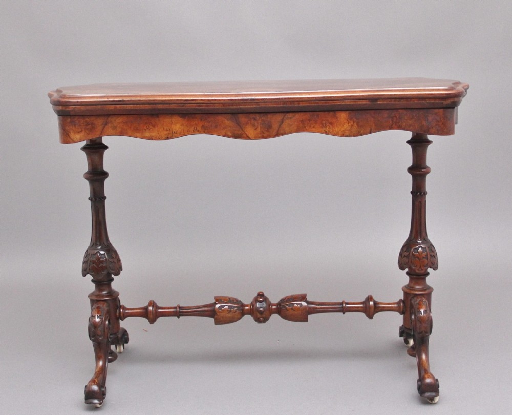 A Victorian burr walnut fold-over card table featuring a serpentine top, carved turned supports, and a stretcher base on castors. View II