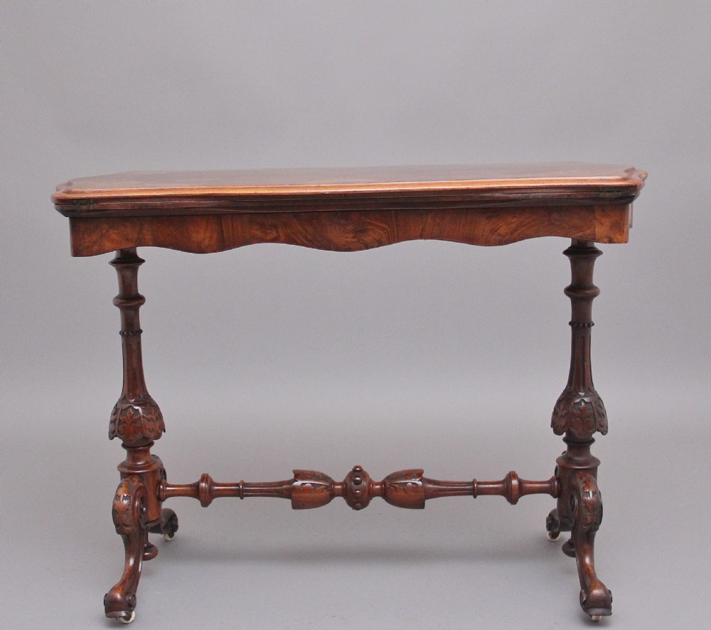 A Victorian burr walnut fold-over card table featuring a serpentine top, carved turned supports, and a stretcher base on castors. View III