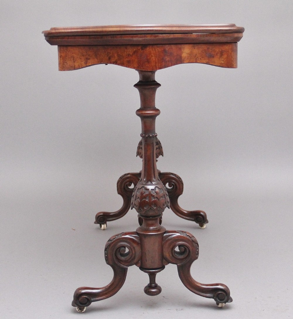 A Victorian burr walnut fold-over card table featuring a serpentine top, carved turned supports, and a stretcher base on castors. View V