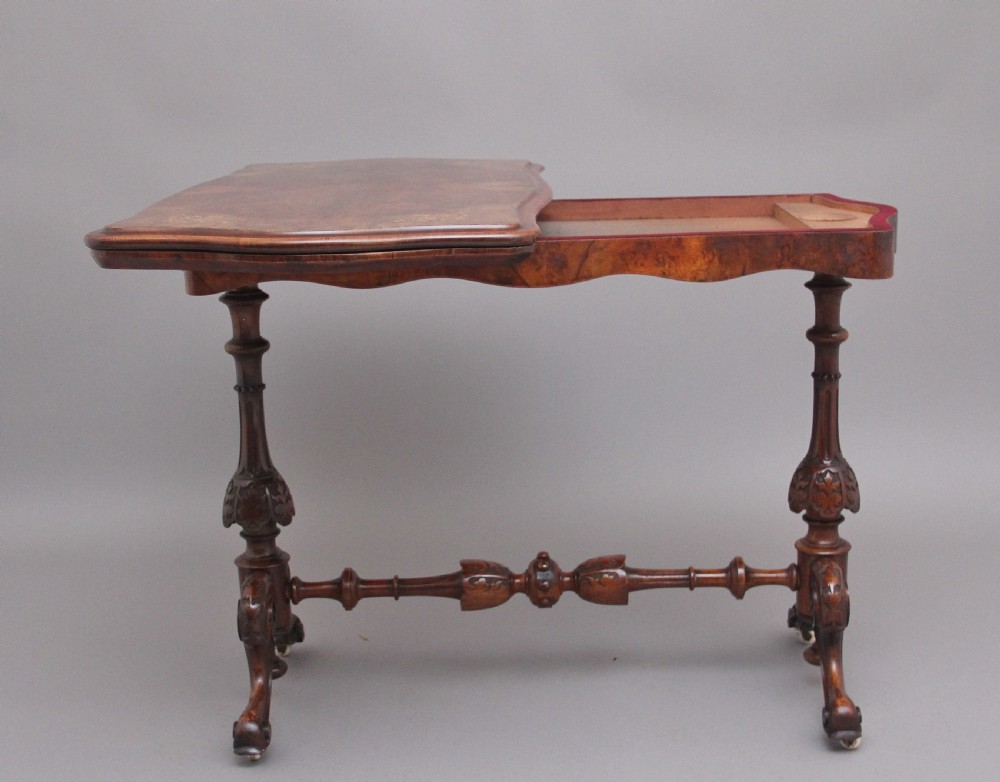 A Victorian burr walnut fold-over card table featuring a serpentine top, carved turned supports, and a stretcher base on castors. View VI