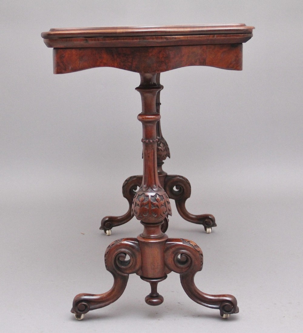 A Victorian burr walnut fold-over card table featuring a serpentine top, carved turned supports, and a stretcher base on castors. View VII