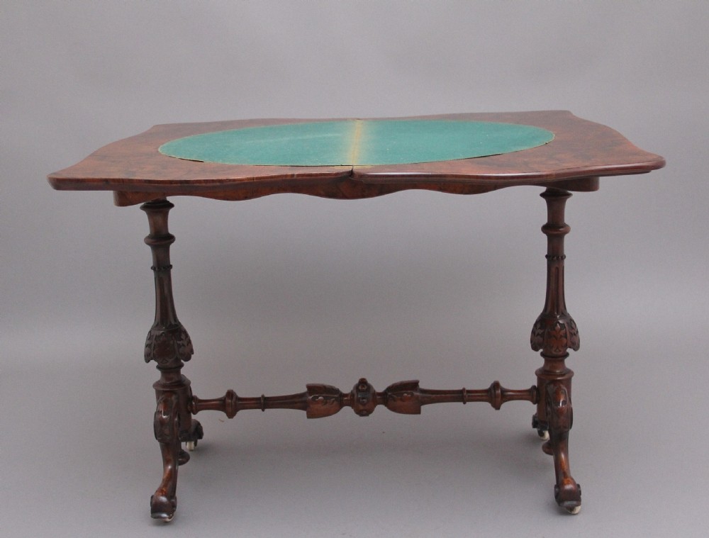 A Victorian burr walnut fold-over card table featuring a serpentine top, carved turned supports, and a stretcher base on castors. View VIII