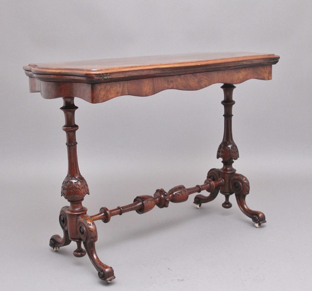 A Victorian burr walnut fold-over card table featuring a serpentine top, carved turned supports, and a stretcher base on castors. View XI
