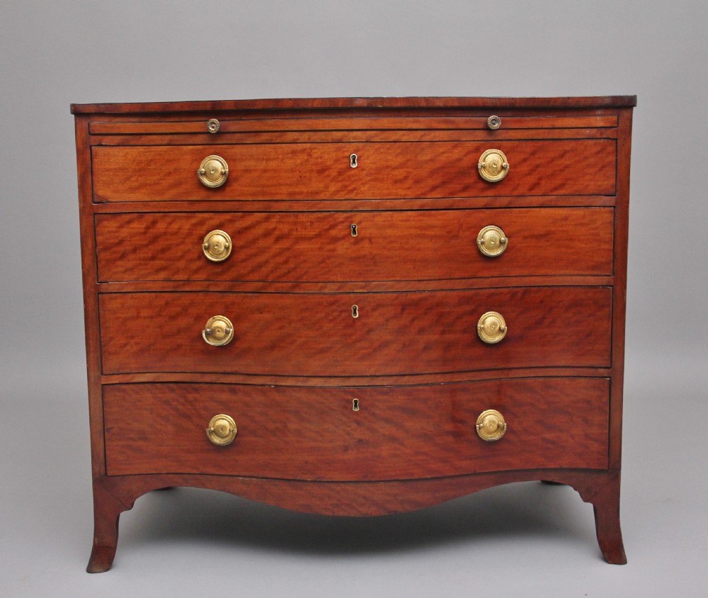 An 18th-century Georgian mahogany chest of drawers with a serpentine front, four graduated drawers, circular brass ring handles, a pull-out brushing slide, and bracket feet.